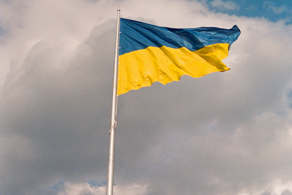 Ukraine's national flag on a flagpole swaying in the wind against slightly dark clouds.