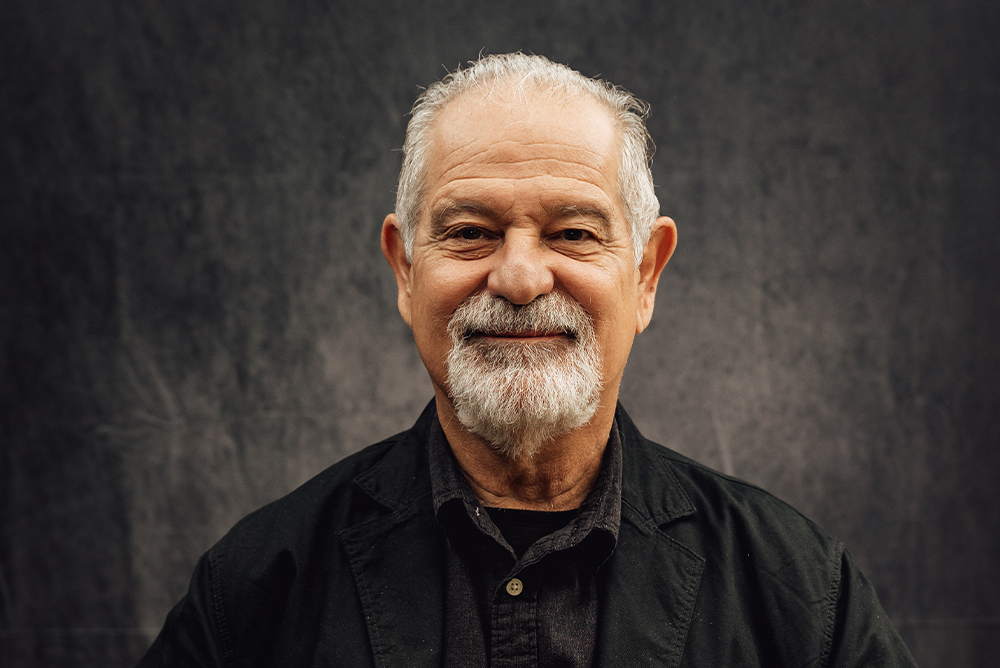 A headshot ofVíctor Zúñiga smiling against a gray-black backdrop. He wears a dark navy shirt.