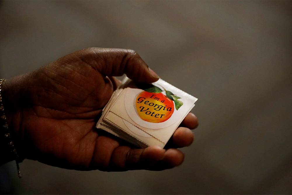 A hand holding a pack of stickers. The stickers read "I'm a Georgia voter" on top of a peach.